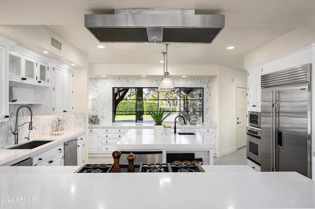 kitchen with built in appliances, white cabinetry, sink, and exhaust hood