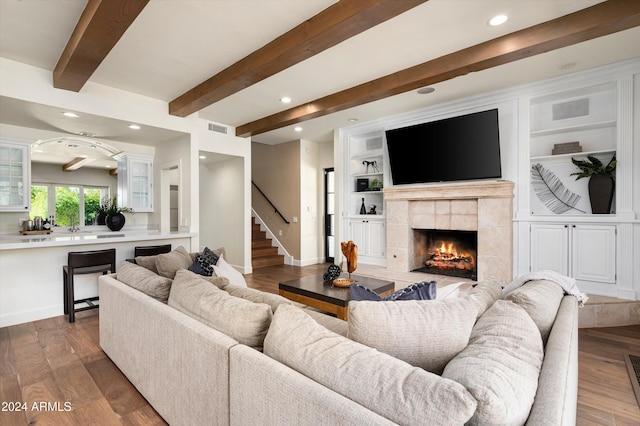 living room with built in shelves, beam ceiling, wood-type flooring, and a tiled fireplace