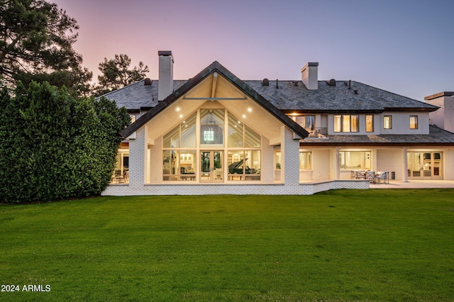 back house at dusk with a patio and a lawn