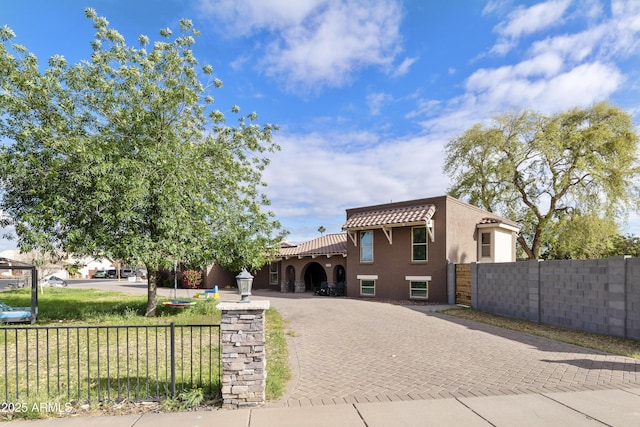 mediterranean / spanish-style home featuring a tile roof, decorative driveway, a fenced front yard, and stucco siding