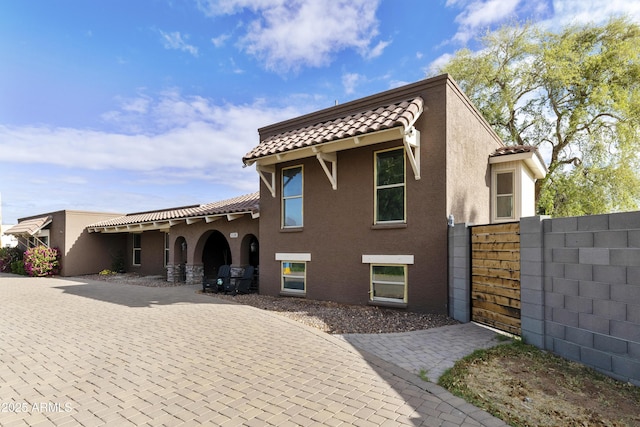 mediterranean / spanish home featuring stucco siding, a tile roof, and fence