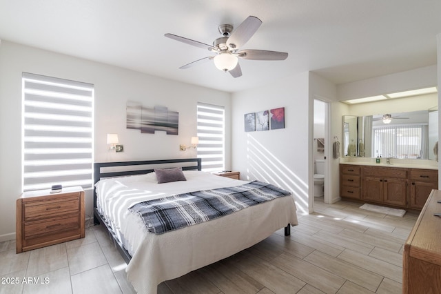 bedroom with ceiling fan, sink, multiple windows, and ensuite bath