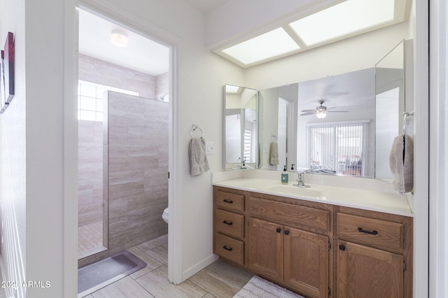 bathroom with a skylight, toilet, vanity, and a tile shower