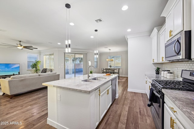 kitchen featuring a center island with sink, sink, appliances with stainless steel finishes, decorative light fixtures, and white cabinetry