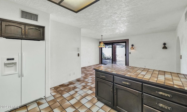 kitchen featuring french doors, dark brown cabinets, tile counters, white fridge with ice dispenser, and hanging light fixtures