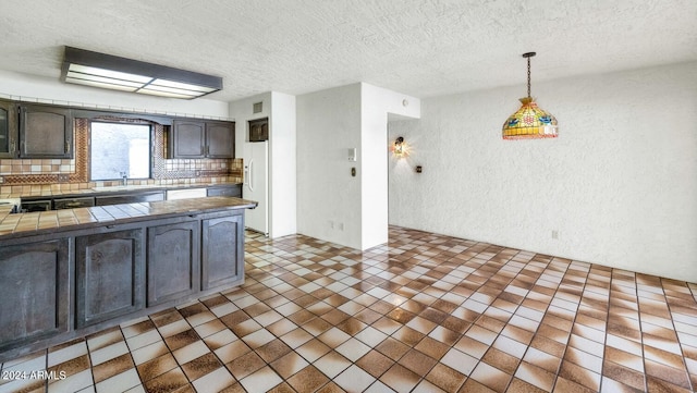 kitchen featuring dark brown cabinetry, sink, tasteful backsplash, pendant lighting, and a textured ceiling