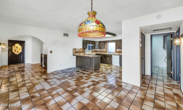 kitchen with dishwasher, backsplash, dark tile patterned floors, a textured ceiling, and dark brown cabinetry