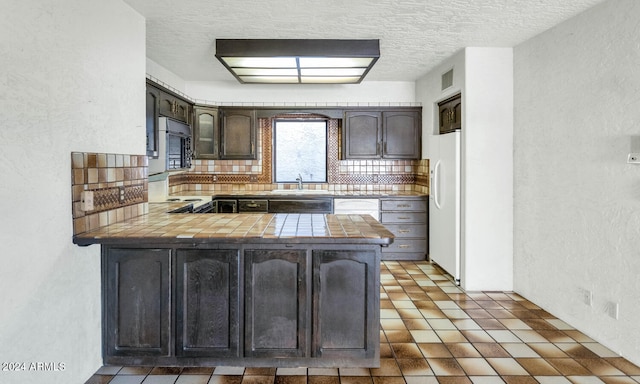 kitchen featuring white appliances, sink, decorative backsplash, dark brown cabinetry, and kitchen peninsula