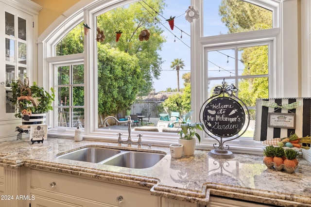 kitchen with plenty of natural light, sink, light stone counters, and white cabinetry