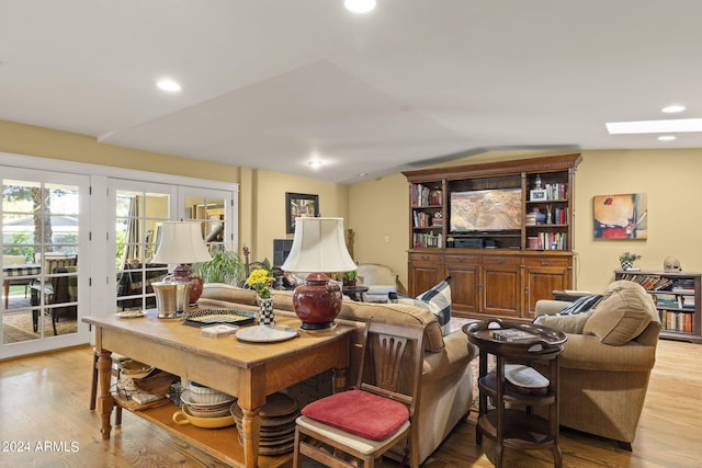 living room with french doors, light hardwood / wood-style floors, and vaulted ceiling with skylight