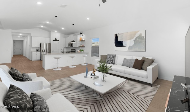 living room with ceiling fan, lofted ceiling, sink, and light hardwood / wood-style floors