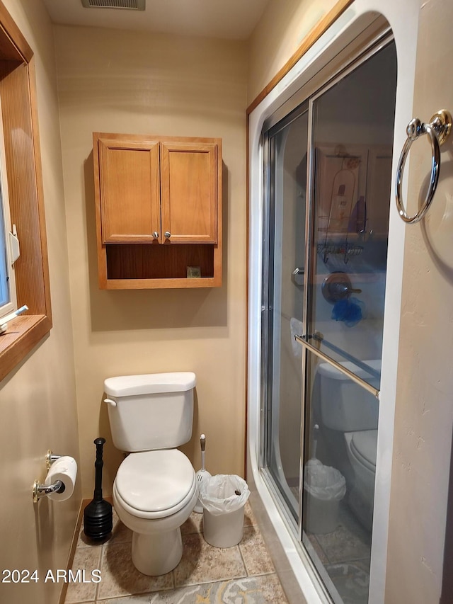 bathroom featuring toilet, tile patterned floors, and a shower with door