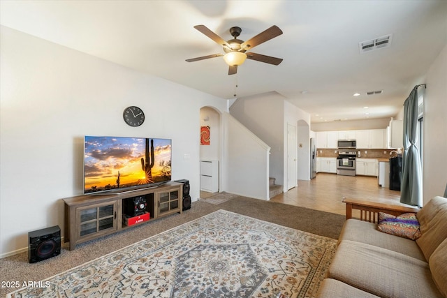 living area featuring visible vents, arched walkways, a ceiling fan, light colored carpet, and stairway