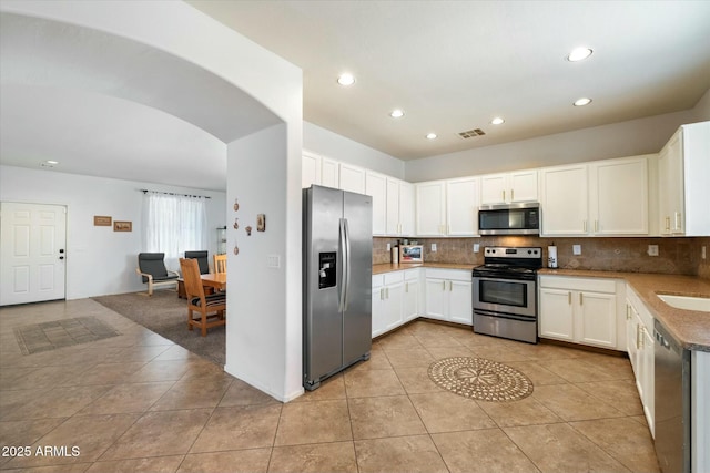 kitchen featuring tasteful backsplash, visible vents, white cabinets, arched walkways, and appliances with stainless steel finishes