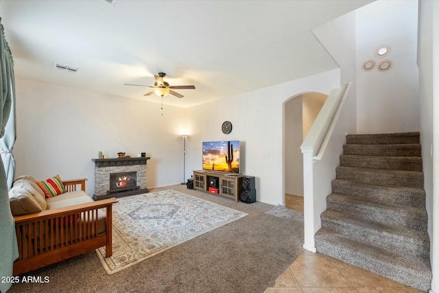 living room with visible vents, light colored carpet, stairway, a stone fireplace, and light tile patterned flooring