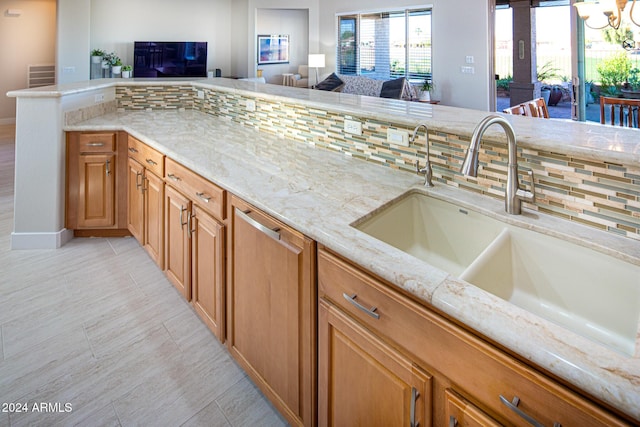 kitchen with tasteful backsplash, light stone counters, a notable chandelier, and sink