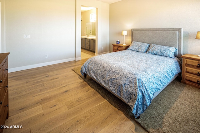 bedroom featuring connected bathroom and light hardwood / wood-style flooring