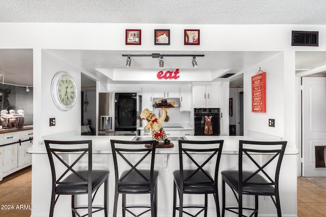 kitchen with stainless steel fridge, kitchen peninsula, oven, white cabinetry, and a kitchen bar