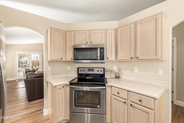 kitchen featuring light wood-style floors, arched walkways, appliances with stainless steel finishes, and light brown cabinetry