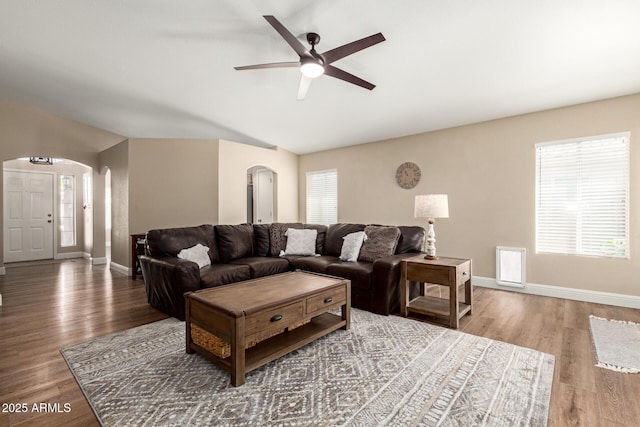 living area with ceiling fan, arched walkways, vaulted ceiling, wood finished floors, and baseboards