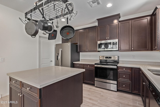 kitchen with light wood-type flooring, dark brown cabinets, a center island, and stainless steel appliances