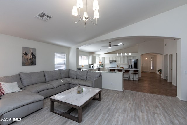 living area with arched walkways, visible vents, ceiling fan with notable chandelier, and vaulted ceiling