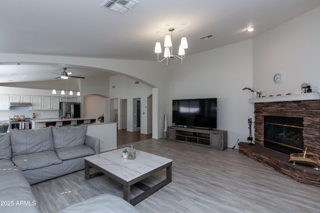 living area featuring visible vents, a stone fireplace, light wood finished floors, and vaulted ceiling
