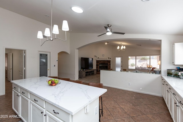 kitchen featuring ceiling fan with notable chandelier, arched walkways, a stone fireplace, lofted ceiling, and open floor plan
