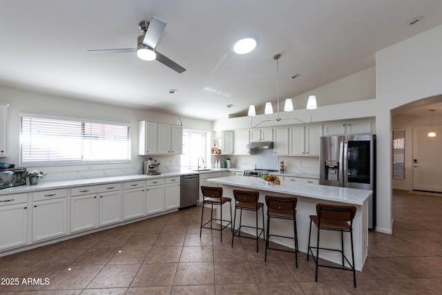 kitchen with a ceiling fan, under cabinet range hood, a kitchen bar, stainless steel appliances, and a sink