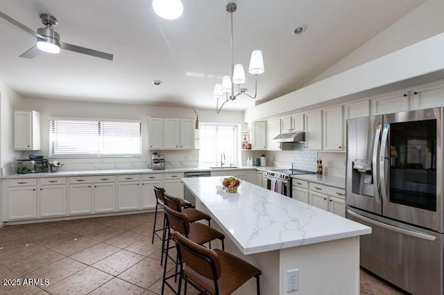 kitchen featuring a sink, appliances with stainless steel finishes, a breakfast bar, under cabinet range hood, and a kitchen island
