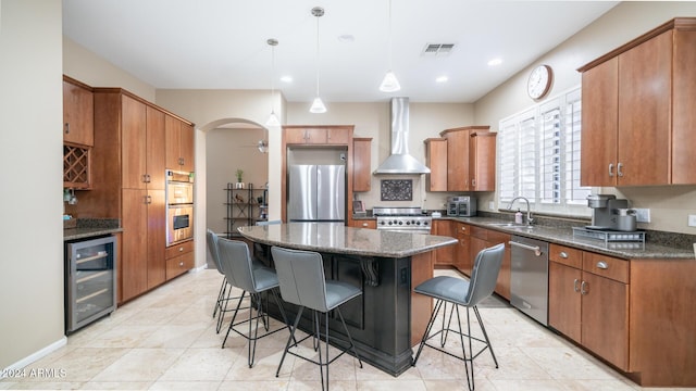 kitchen featuring ceiling fan, wall chimney range hood, wine cooler, a kitchen island, and appliances with stainless steel finishes