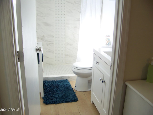 bathroom featuring tiled shower, hardwood / wood-style flooring, vanity, and toilet