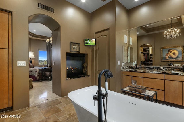 bathroom with vanity, a multi sided fireplace, a notable chandelier, and a bathtub