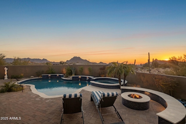 pool at dusk featuring a mountain view, a fire pit, a patio, and an in ground hot tub