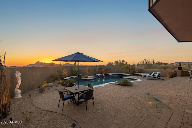 pool at dusk with an in ground hot tub and a patio