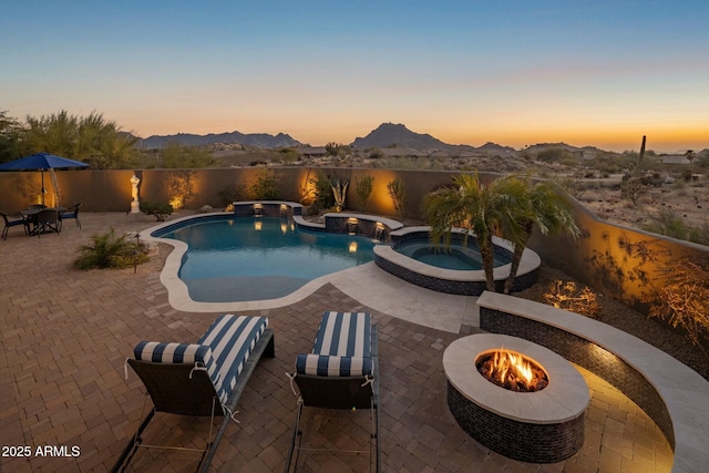 pool at dusk featuring an in ground hot tub, a mountain view, a patio area, and a fire pit