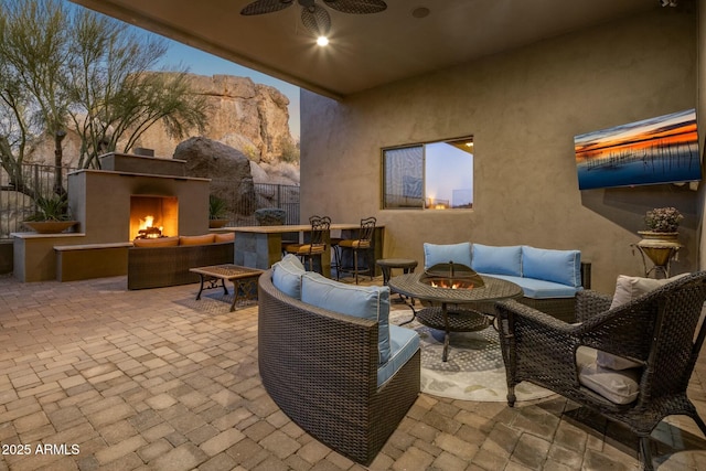 patio terrace at dusk with ceiling fan, an outdoor living space with a fireplace, and a mountain view