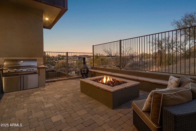 patio terrace at dusk featuring area for grilling, a fire pit, and an outdoor kitchen