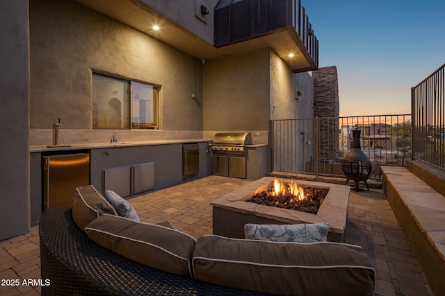 patio terrace at dusk featuring area for grilling, an outdoor fire pit, and a grill