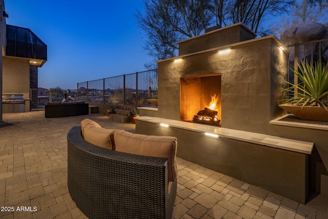 patio terrace at dusk featuring exterior fireplace and a grill