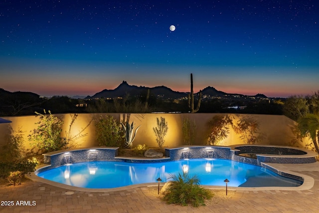 pool at dusk with pool water feature, an in ground hot tub, a mountain view, and a patio area