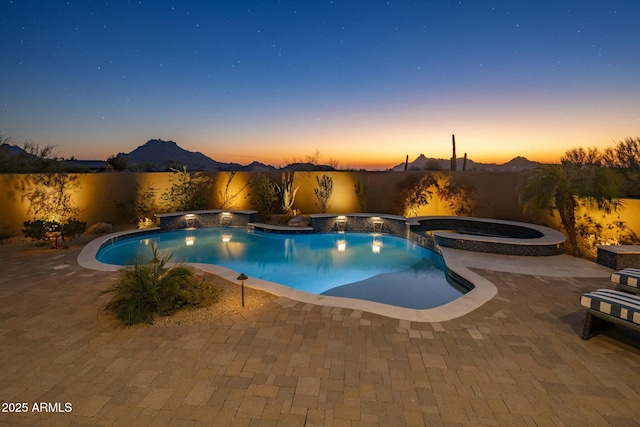 pool at dusk with an in ground hot tub, pool water feature, a mountain view, and a patio