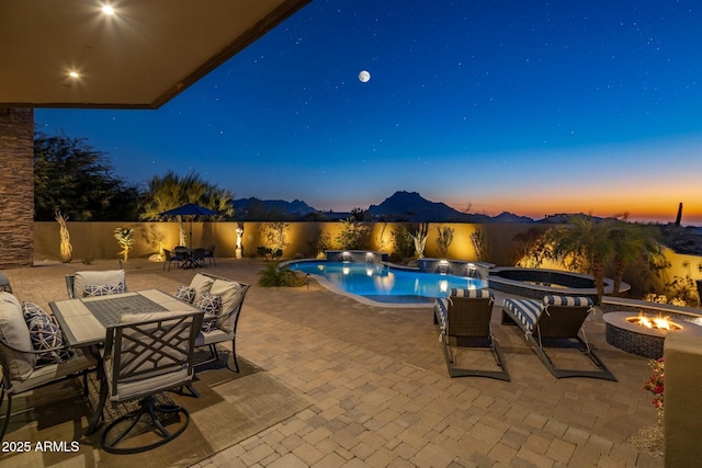 pool at dusk featuring an in ground hot tub, a mountain view, a patio area, and a fire pit