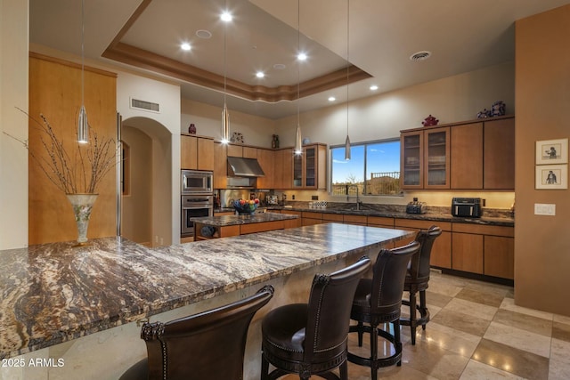 kitchen with dark stone countertops, appliances with stainless steel finishes, pendant lighting, and a tray ceiling