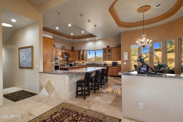 kitchen featuring appliances with stainless steel finishes, a kitchen breakfast bar, a raised ceiling, kitchen peninsula, and dark stone counters