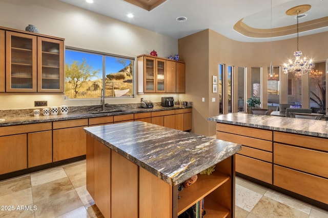 kitchen featuring sink, dark stone countertops, a kitchen island, a raised ceiling, and a chandelier