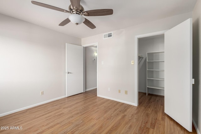 unfurnished bedroom featuring light wood-type flooring, visible vents, a spacious closet, and baseboards