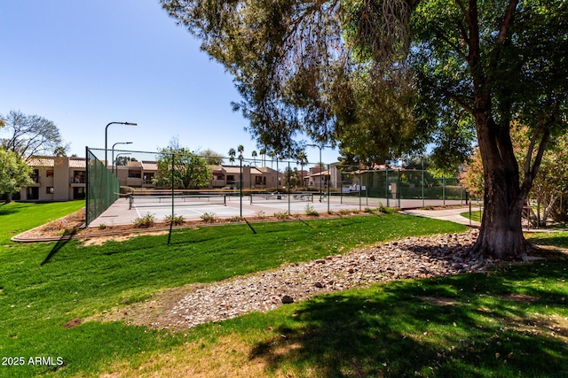 view of home's community featuring a tennis court, a lawn, and fence