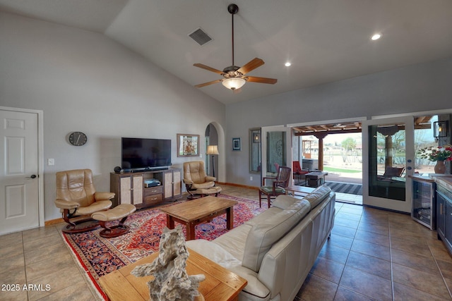 tiled living area with beverage cooler, visible vents, arched walkways, a ceiling fan, and high vaulted ceiling