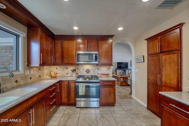 kitchen with arched walkways, stainless steel appliances, a sink, visible vents, and backsplash